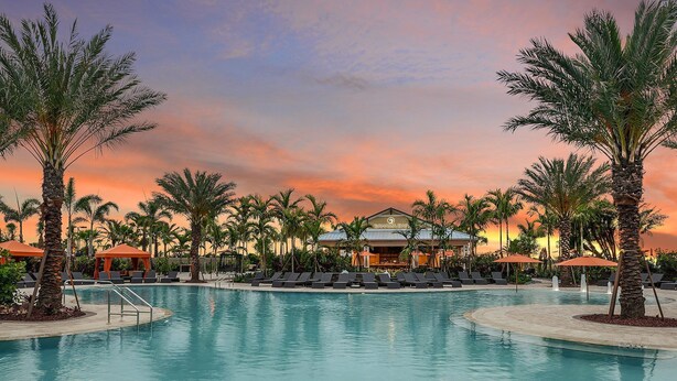 Ein Pool in einem Resort mit Liegestühlen und Sonnenschirmen, umgeben von Palmen und einem Gebäude mit der Aufschrift "Bahama Bar".