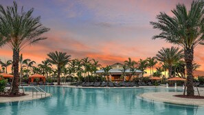 Zwembad van een resort met ligbedden en parasols, omgeven door palmbomen en een gebouw met de tekst 