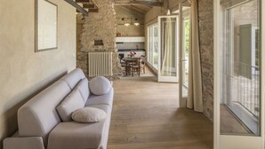 Ein gemütliches Interieur mit Steinwand, Holzboden, einer Couch, einem Esstisch mit Stühlen und einer Küchenzeile.
