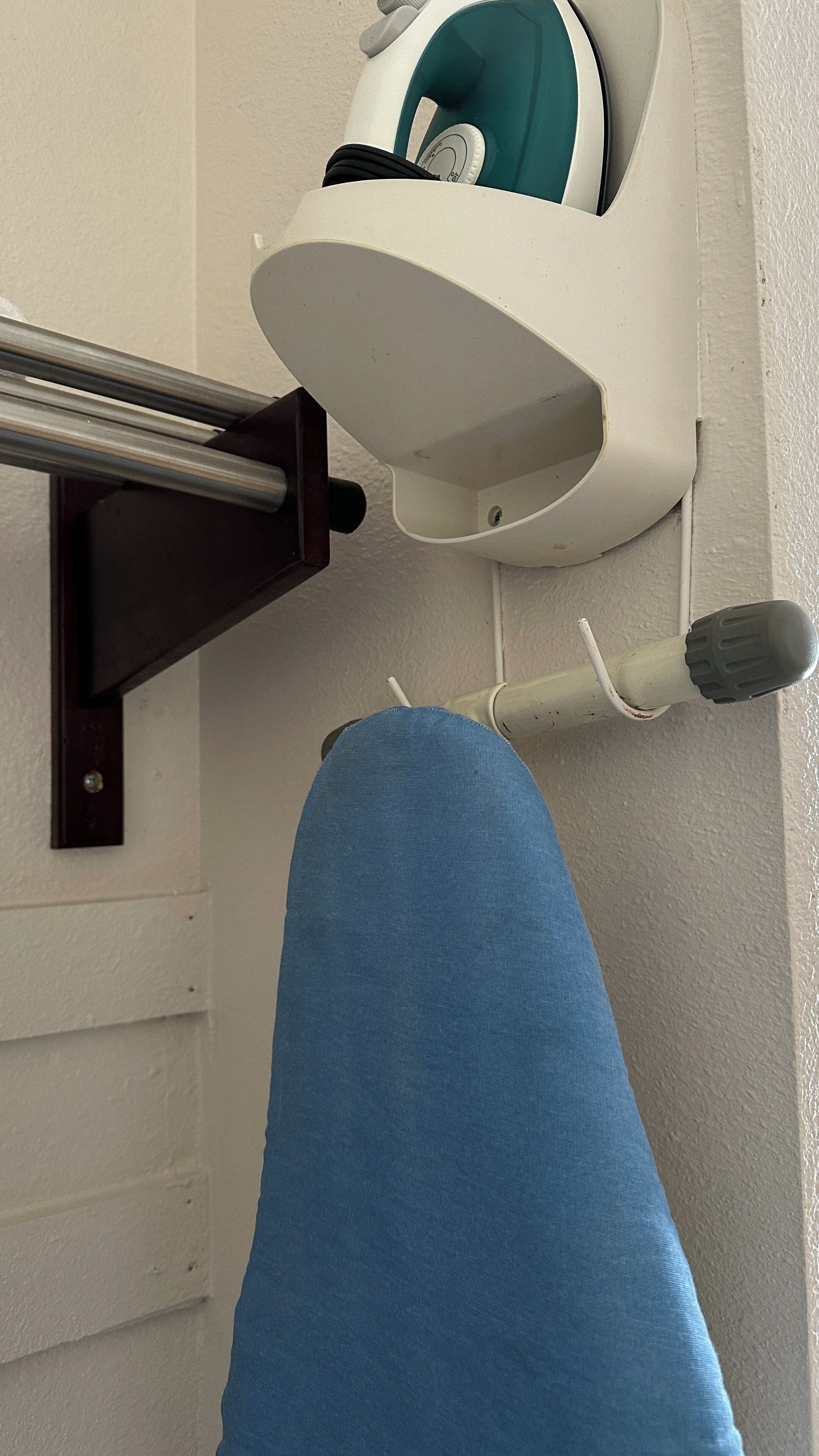 A bathroom with a white wall, a towel rack, a towel, and a white and teal showerhead.