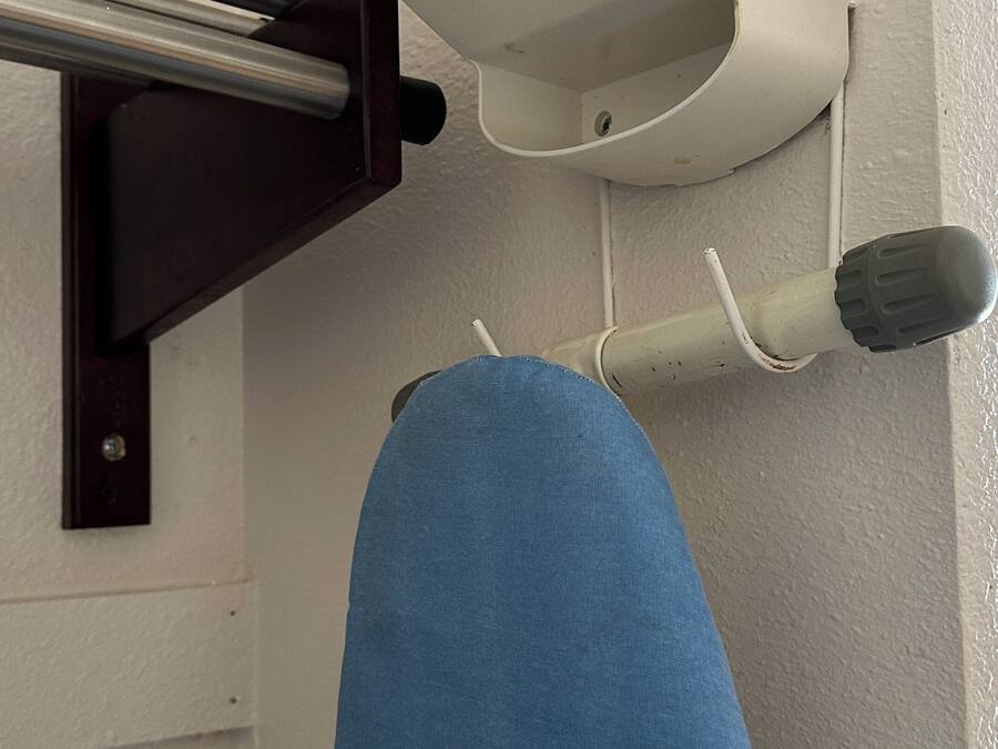 A bathroom with a white wall, a towel rack, a towel, and a white and teal showerhead.