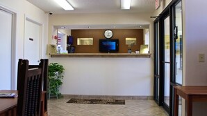 A reception area with a reception desk, a clock, and a digital screen displaying a message. - Carom Inn Denham Springs-Baton Rouge (Denham Springs)