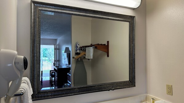 A bathroom with a large mirror, a hairdryer, and an ironing board.