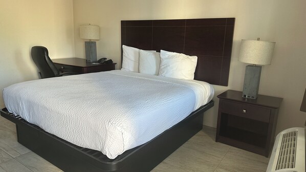 A hotel room with a large bed, a dark headboard, two bedside tables with lamps, and a chair.