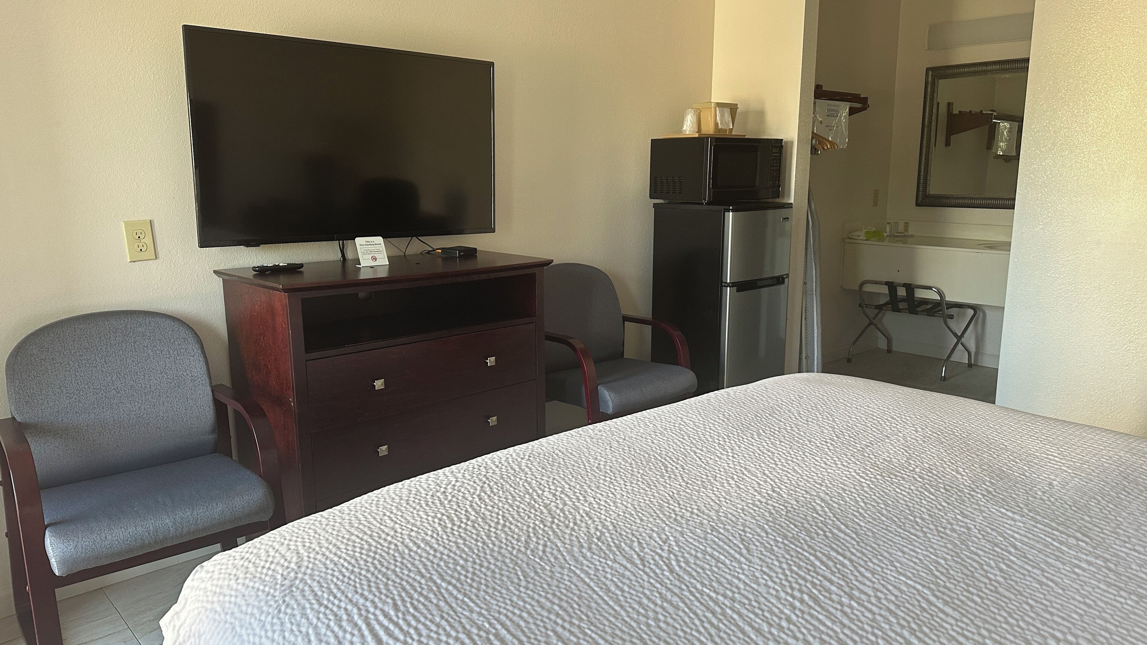 A hotel room with a bed, a desk with a television, a refrigerator, and a chair.