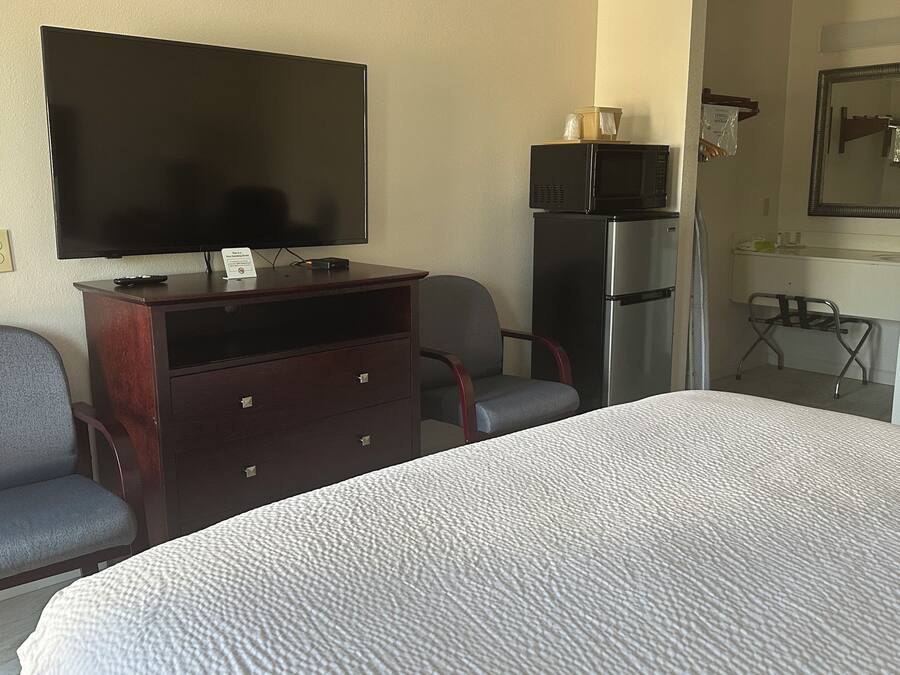 A hotel room with a bed, a desk with a television, a refrigerator, and a chair.