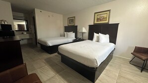 A hotel room with two beds, a desk, a chair, and a bathroom visible in the background. - Carom Inn Denham Springs-Baton Rouge (Denham Springs)
