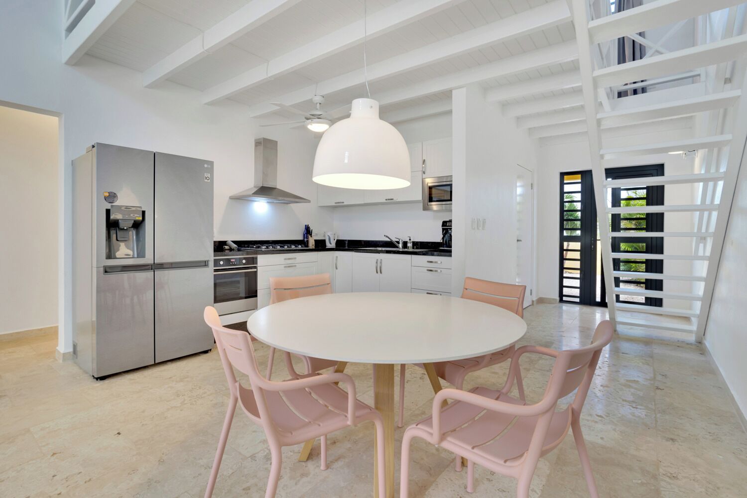 A modern kitchen with a stainless steel refrigerator, a built-in oven, and a large white dining table with pink chairs.