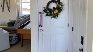 A white door with a wreath, a fire exit sign, and a staircase leading to another room.