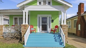 Una casa con fachada verde, un porche azul y dos sillas Adirondack rojas.