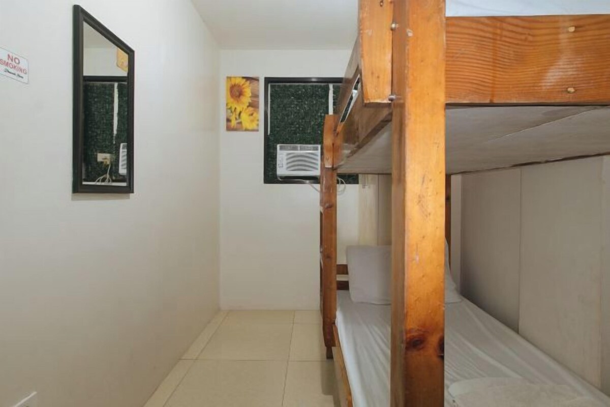 Un couloir étroit avec des lits superposés, un miroir et une fenêtre décorée d’un motif de tournesol.