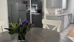 Ein Esstisch mit Blumen, eine Küche mit grauen Schränken und eine Glastür, die in einen anderen Raum führt.