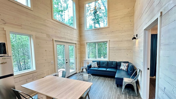 L’intérieur d’une cabane comprend un coin repas, un canapé et de grandes fenêtres donnant sur la forêt.