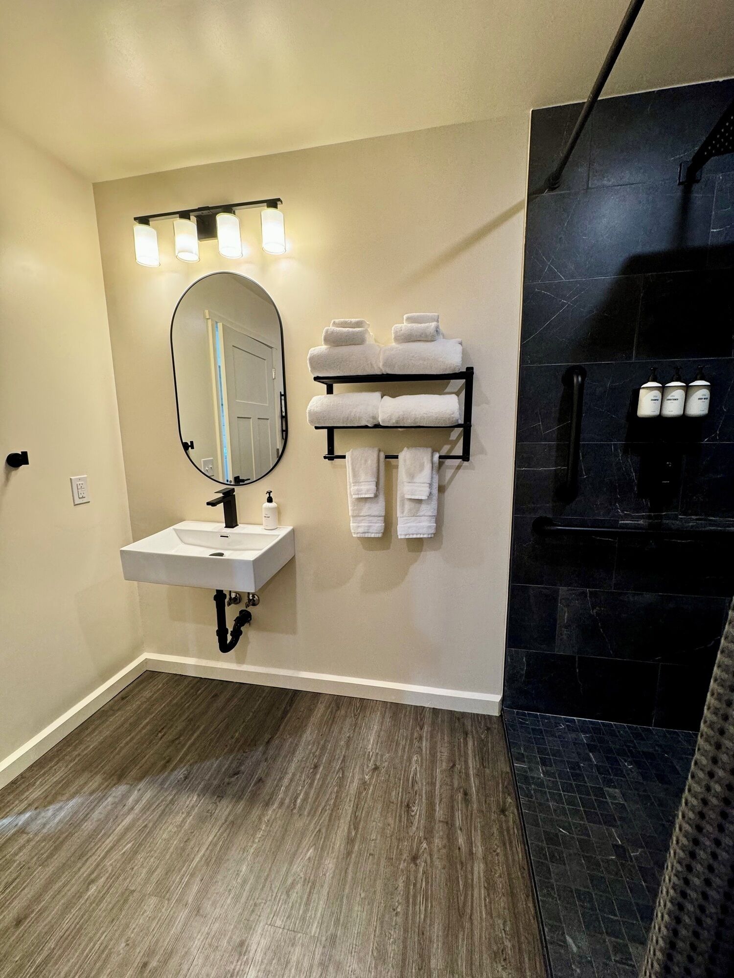 A bathroom with a sink, mirror, towel rack, and black tiled shower area.