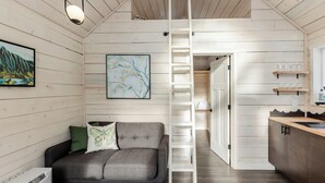 Een gezellige kamer met een grijze bank, een ladder, een schilderij en een houten kast.