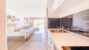 Ein modernes Schlafzimmer mit einem großen Bett, Nachttischen und Blick zur Küche.
