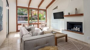 Un salon moderne avec un canapé, une table basse et une cheminée. De grandes fenêtres offrent une vue sur l’extérieur.