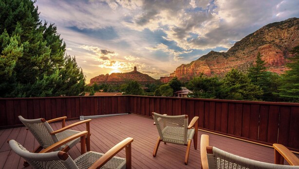 Une terrasse dotée de chaises en osier et d’une clôture en bois, offrant une vue sur un paysage montagneux.
