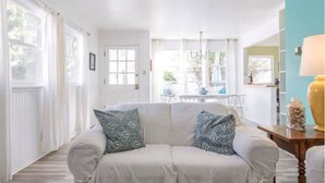 A cozy living room with a white sofa, patterned cushions, and a view of a dining area through large windows. - Ventura Beach 1 (Ventura)