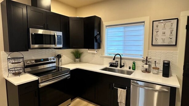 A modern kitchen with black cabinets, stainless steel appliances, a window with blinds, and a framed menu on the wall. - 2-bedroom vacation home just 13 minutes drive to Moda Center (Vancouver)