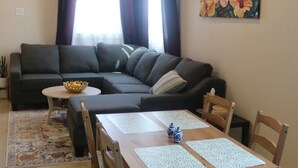 A living room with a sofa, a dining table with chairs, a small round table with a bowl, and a painting on the wall. - 2-bedroom vacation home just 13 minutes drive to Moda Center (Vancouver)