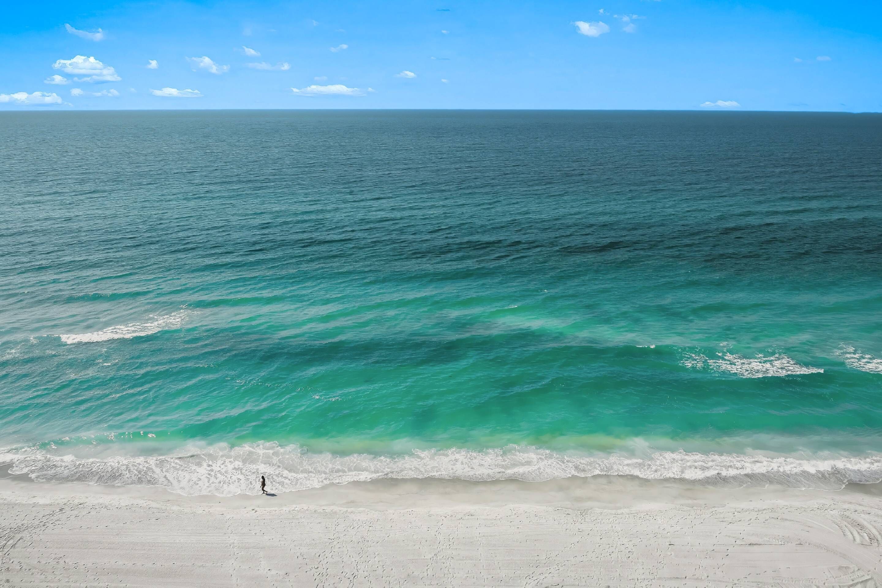 A beach with clear turquoise waters and a person walking along the shore.