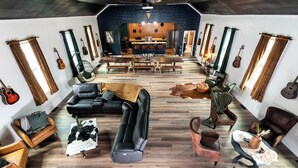A spacious living area with a central seating area, a kitchen in the background, and various musical instruments displayed on the walls. - Cozy, sleeps 20 retreat in Auburn game area and large family entertaining (Auburn)