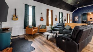 A living room with a leather sofa, two armchairs, a coffee table, and a black rug. There are guitars hanging on the wall and a blue cabinet with a bowl on top. - Cozy, sleeps 20 retreat in Auburn game area and large family entertaining (Auburn)