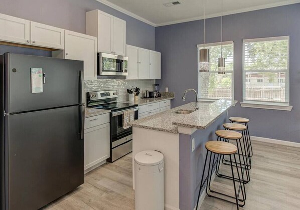 A modern kitchen with white cabinets, stainless steel appliances, and a granite countertop.