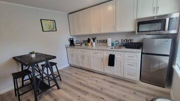A modern kitchen with white cabinets, a stainless steel refrigerator, and a wooden dining table with stools.