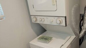 Máquina de lavar roupa compacta e branca, com painel de comandos e um pequeno objeto decorativo verde em cima.