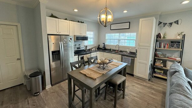 Una cocina moderna con armarios blancos, un refrigerador de acero inoxidable y una mesa de comedor con un mantel individual.