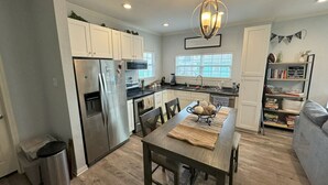Una cocina moderna con armarios blancos, electrodomésticos de acero inoxidable y un comedor con mesa de madera.