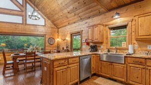 A wooden cabin kitchen with a large island, wooden cabinets, and a dishwasher. - River Front! Pool Table! Riverfront Fire Pit! Hot Tub! BlueRidgeScenicRailway! (Blue Ridge)