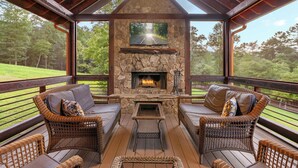 A covered outdoor area with wicker furniture, a stone fireplace, and a television screen. - River Front! Pool Table! Riverfront Fire Pit! Hot Tub! BlueRidgeScenicRailway! (Blue Ridge)