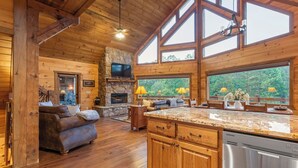 A spacious wooden cabin interior with a stone fireplace, a large kitchen with granite countertops, and a cozy seating area. - River Front! Pool Table! Riverfront Fire Pit! Hot Tub! BlueRidgeScenicRailway! (Blue Ridge)