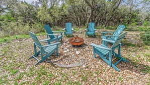 Quatre chaises Adirondack bleues sont disposées en cercle autour d’un foyer central, dans un cadre naturel.
