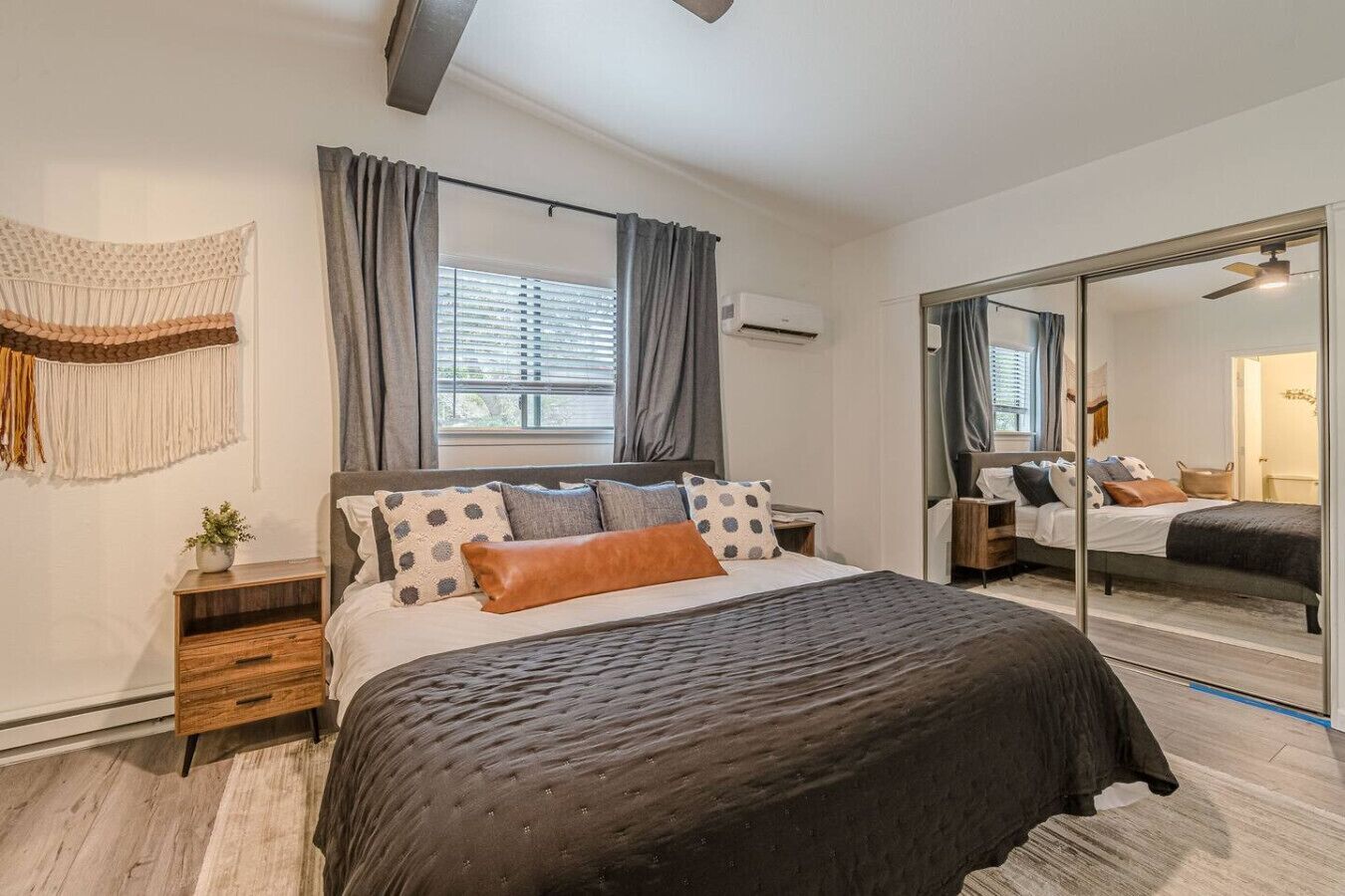 Een moderne slaapkamer met een groot bed, een nachtkastje, een spiegel en een raam met gordijnen.