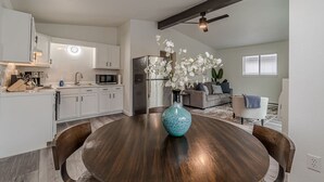 Une cuisine moderne avec des meubles blancs, un réfrigérateur en acier inoxydable et un coin repas comprenant une table ronde en bois et des chaises.