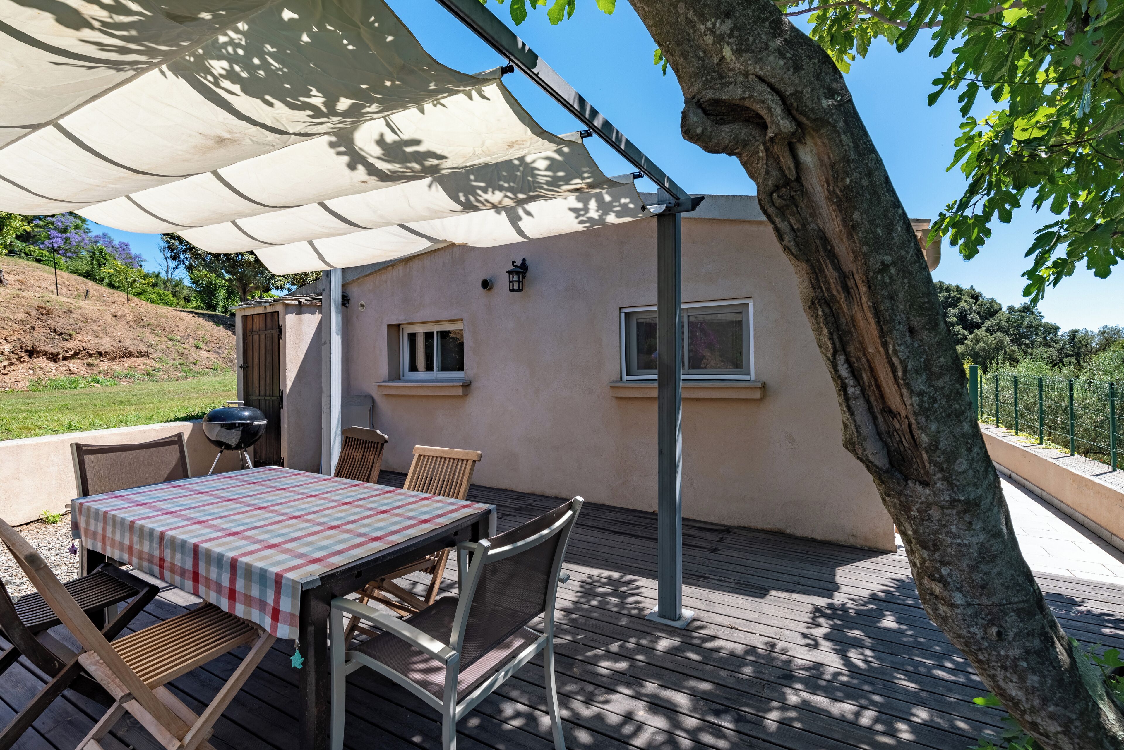 Un patio al aire libre con mesa y sillas, una parrilla y un área cubierta con un árbol.