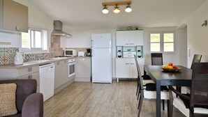 Eine moderne Küche mit weißen Schränken, einem eingebauten Ofen, einer Mikrowelle und einem Kühlschrank. Ein Esstisch mit Stühlen und einer Obstschale steht daneben.
