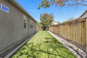 A backyard with a well-maintained lawn, a wooden fence, and a house with a stucco exterior.