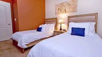A hotel room with two single beds, each with white bedding and blue pillows, a wooden headboard, and a nightstand with a lamp.