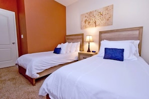 Une chambre d’hôtel avec deux lits simples, chacun doté de draps blancs et d’oreillers bleus, d’une tête de lit en bois et d’une table de chevet avec une lampe.