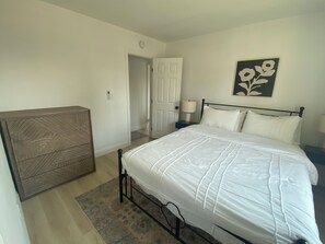 Ein Schlafzimmer mit Bett, Nachttisch, Kommode und einer Tür zu einem anderen Raum.