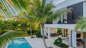 A modern house with a pool, outdoor seating, and lush greenery. - New Lake Front Villa in Golf and Beach Resort (Punta Cana)