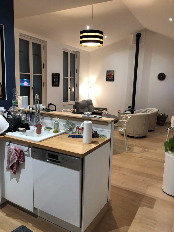 A modern kitchen with a central island, a dishwasher, and a dining area with a sofa and chairs. - Maison Centre de La Tremblade (la tremblade)