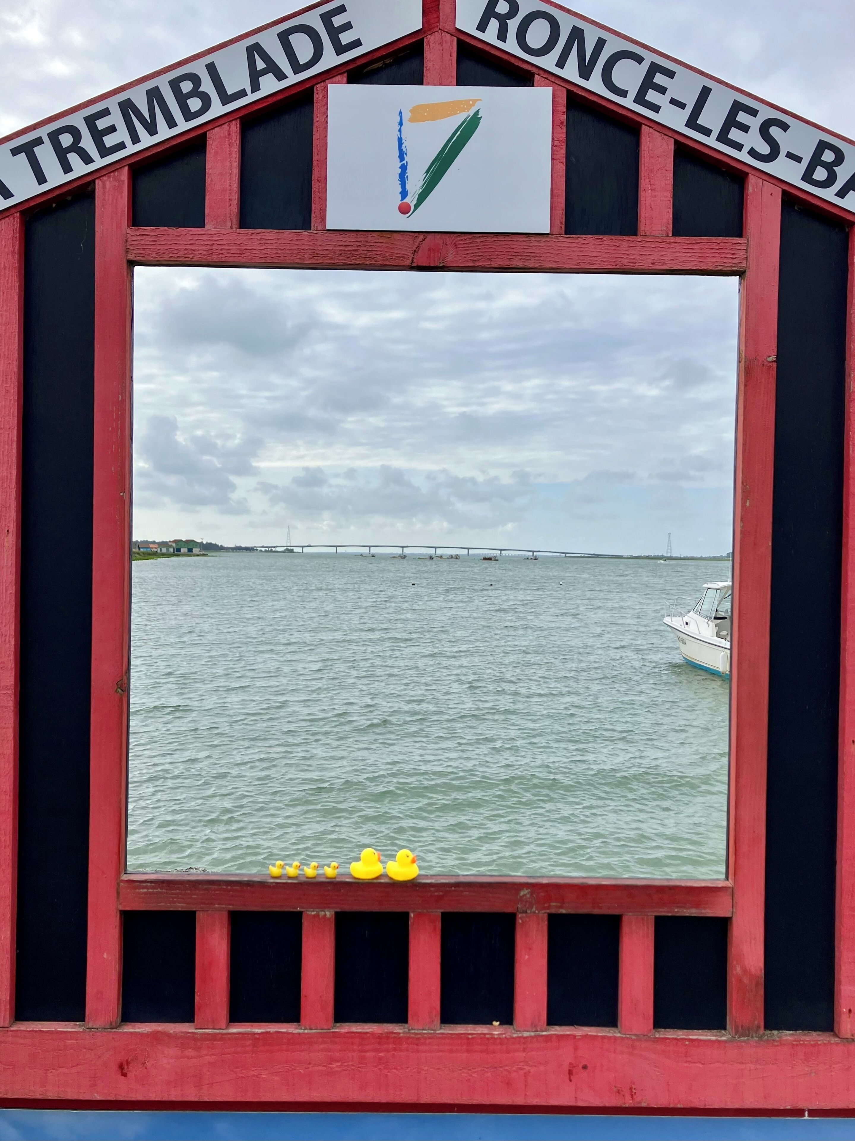 A view through a window with a sign reading 'TREMBLADE' and 'RONCE-LES-BA' with a bridge in the background.