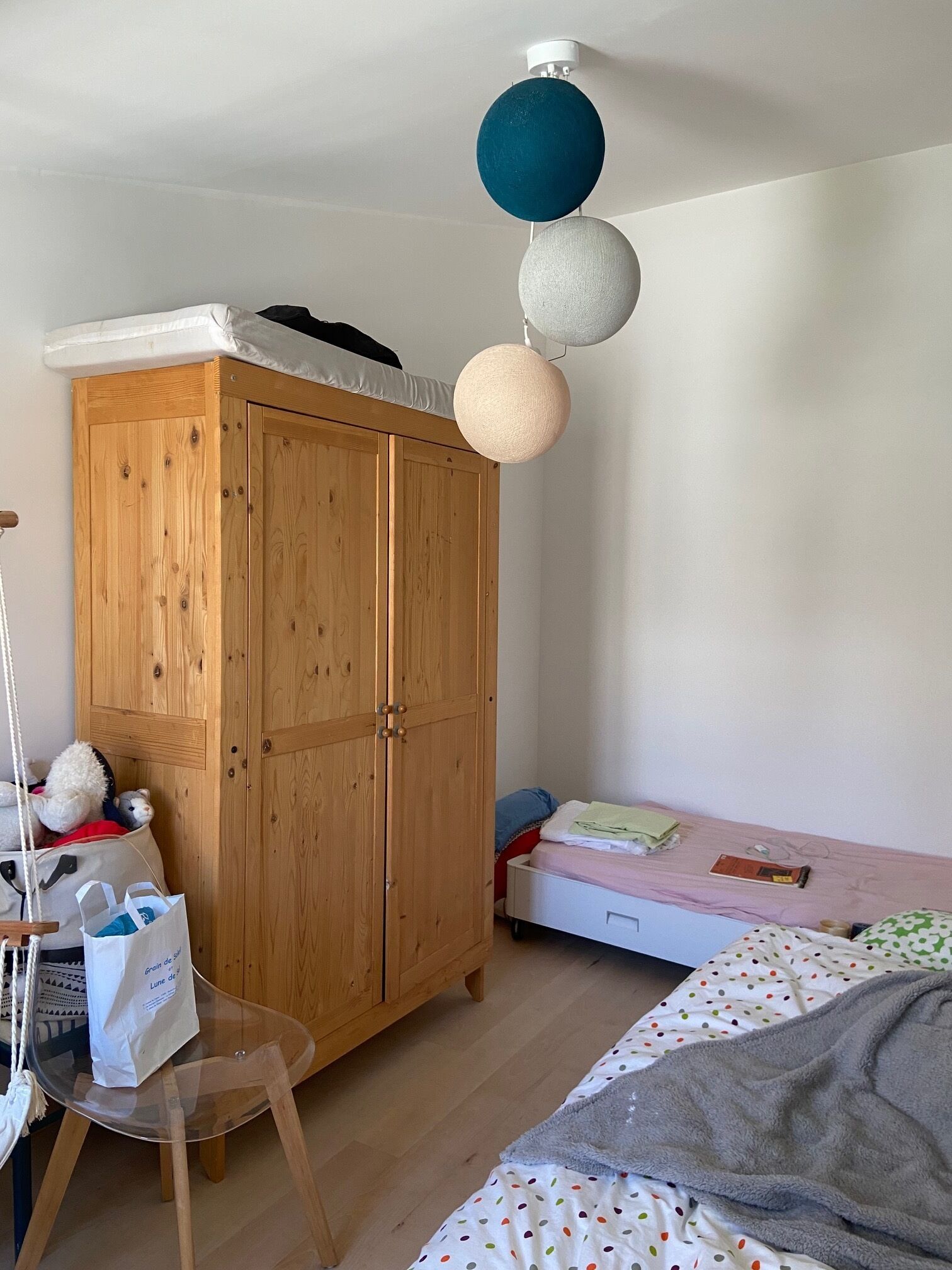 Quarto com armário de madeira, cama com colcha de poás, cadeira pendente e luminárias esféricas no teto.