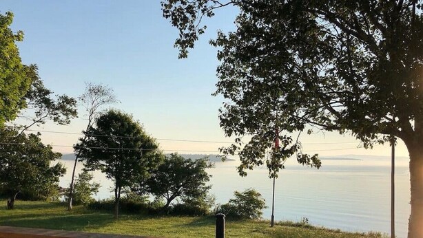 Vista desde un balcón con barandilla, sobre un lago rodeado de árboles y un cielo despejado.